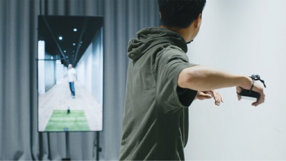 A man playing catch by throwing a virtual ball on his smartphone to the person displayed on the monitor in front of him.