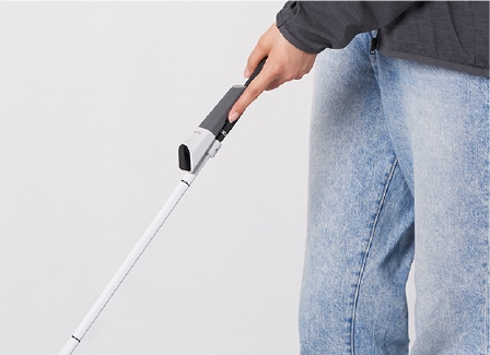 A small sensing device attached to the handle of a white cane.