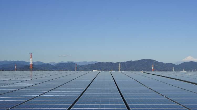 Wide landscape shot showing a large array of solar panels stretching into the distance, with hills in the background