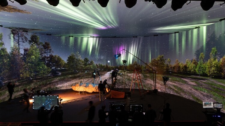 Wide shot of virtual production studio set decorated to look like outdoor location at night, with camera crew, various lights, and virtual background showing night sky with stars and aurora