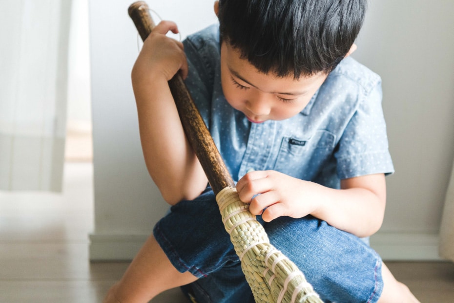 Photo of a child holding a the broom for children in his hand and looking at it