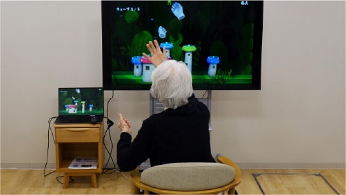 Image of a resident experiencing a rehabilitation game using sensing technology in a nursing home.