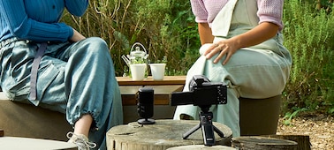 Usage image of two people sitting outdoors with a microphone in front of them, and a camera nearby with receiver attached