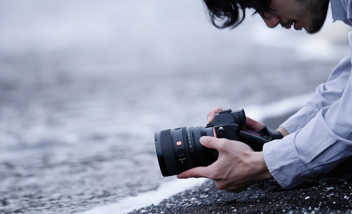 A male photographer is seen kneeling at the water's edge, capturing photos at an angle that suggests he might be immersed in the sea.