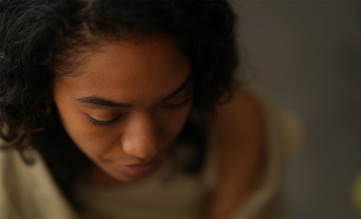 A portrait captured from above, showcasing a black woman with long lashes looking downwards in a softly lit interior.