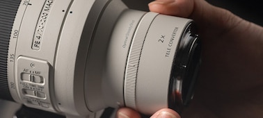 Usage image showing user holding lens with 2.0× teleconverter mounted