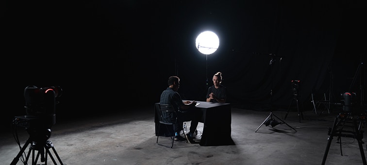 Image of two men talking face to face in a room with one light