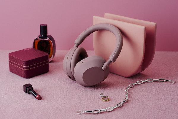 The WH-1000XM5 wireless headphones in Smoky Pink sat on a pink carpet next to beauty accessories.