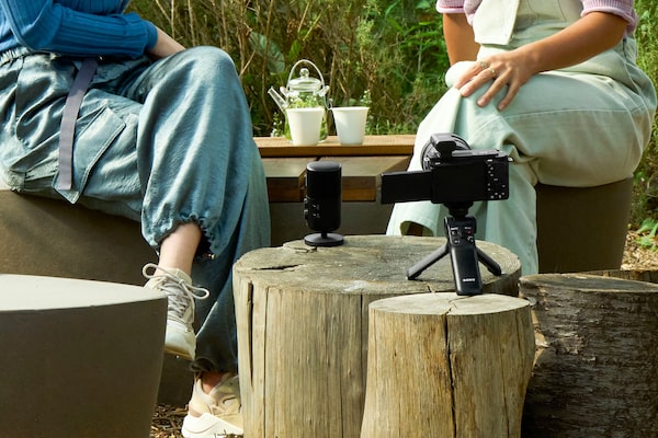 Usage image of two people sitting outdoors with a microphone in front of them, and a camera nearby with receiver attached