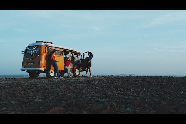 Example image of four men and women chatting around an orange campervan