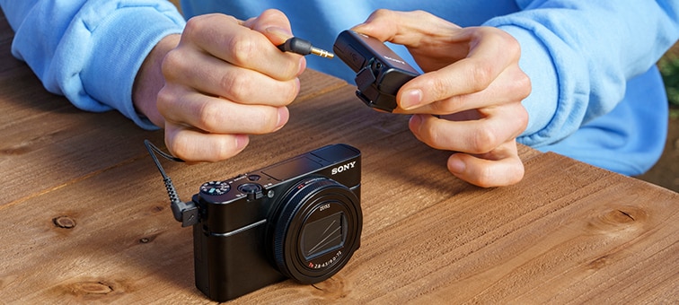 A person connecting the ECM-W2BT with a cable to a compatible camera via a 3.5 mm stereo mini-jack