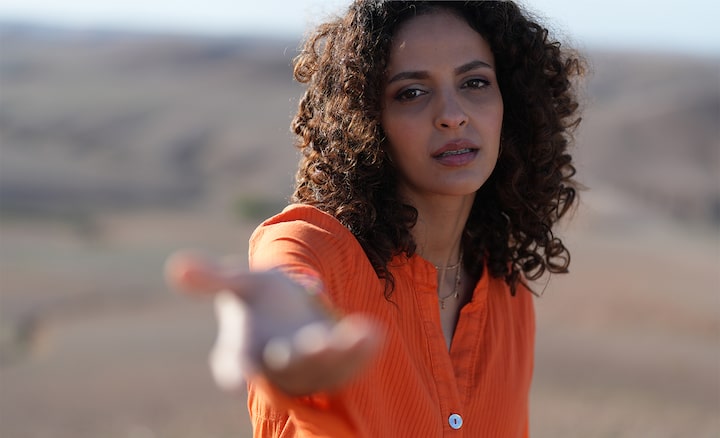 Example image of a female model stretching her right arm towards the camera, with bokeh foreground and background