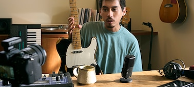 Usage image of a man holding a guitar and speaking into the microphone nearby, while looking at the camera with receiver attached