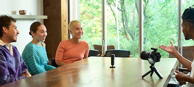 Usage image of a microphone placed in the center of a table with four people conversing around the microphone